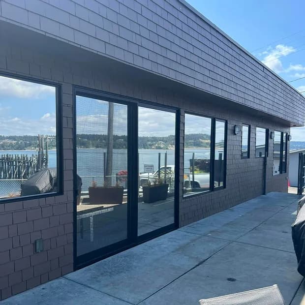 Waterfront building with black-framed sliding glass walls treated with solar window film, overlooking the bay
