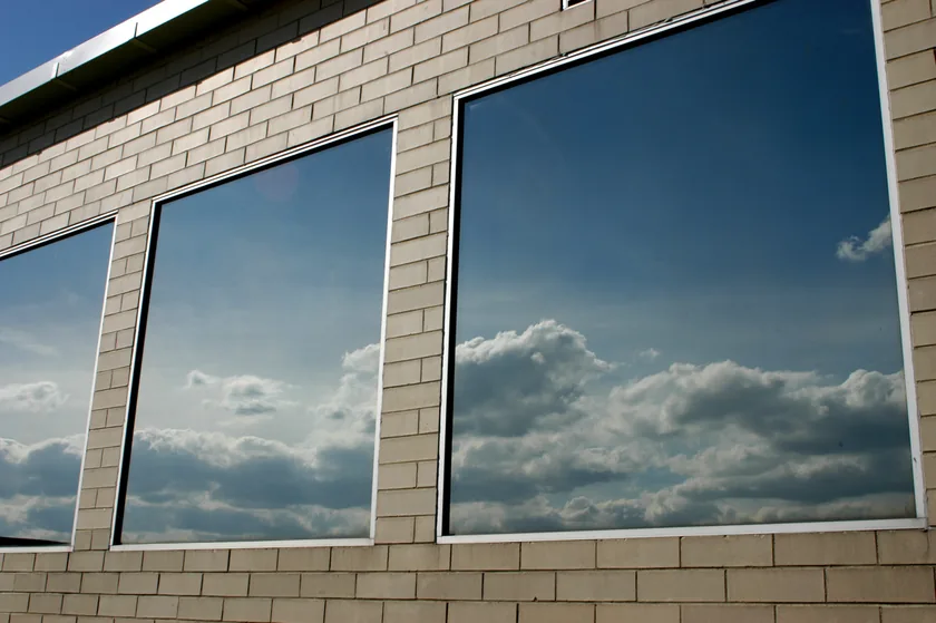 Commercial building windows finished with reflective solar-control film, mirroring a blue, cloud-filled sky